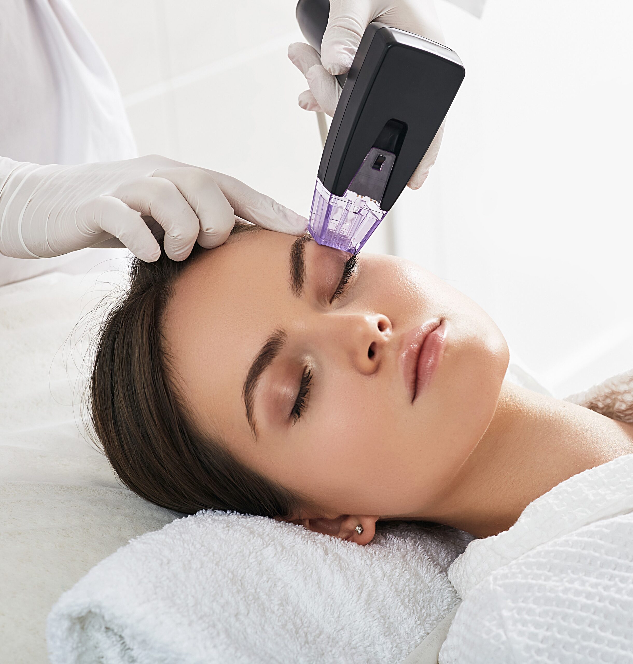 Brown haired woman receiving radiofrequency lifting procedure around eyes for her face skin rejuvenation at aesthetic cosmetology center